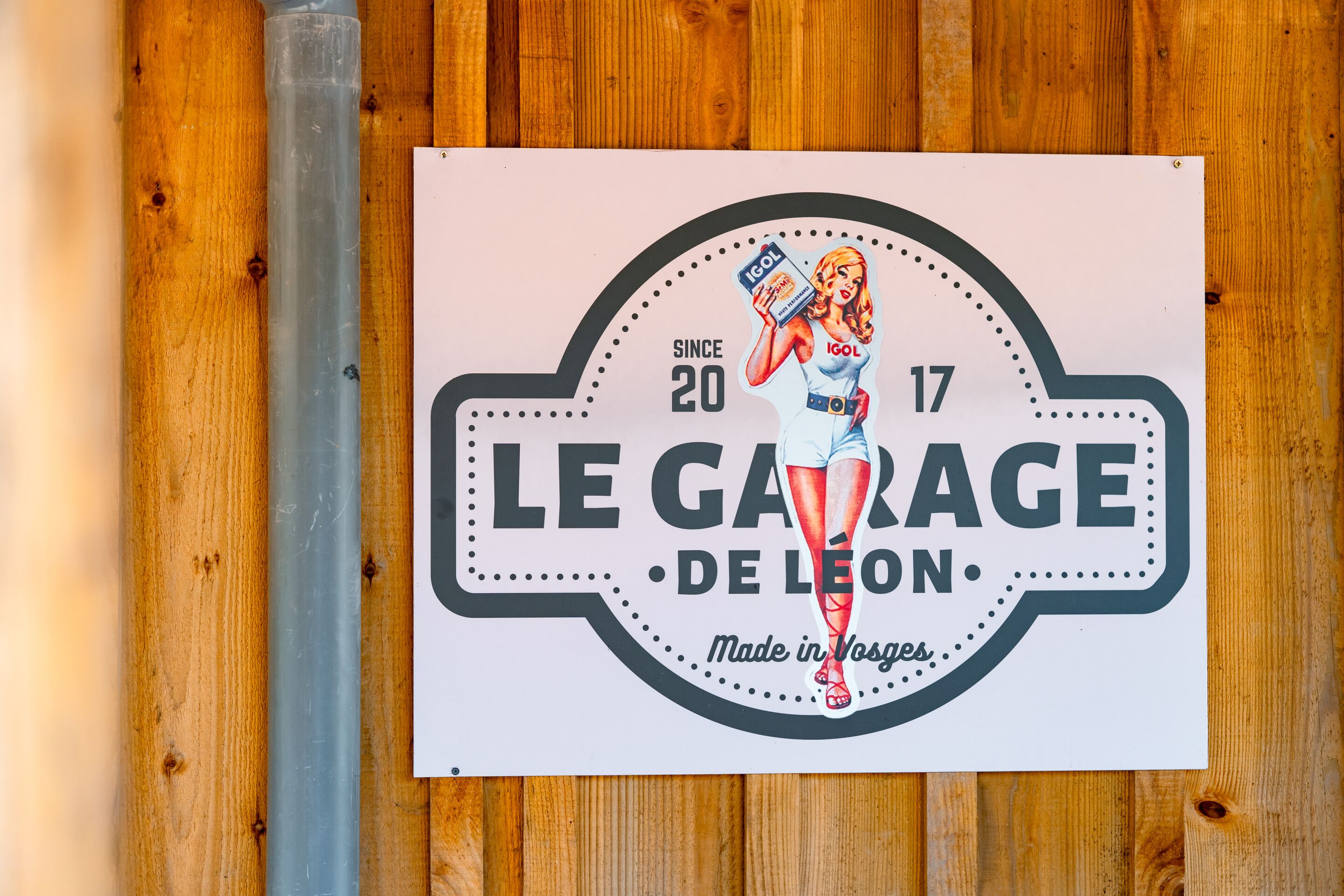 A vintage-style sign with a woman holding a product, 'LE GARAGE DE LÉON' text, and 'SINCE 1920' on a wooden background.
