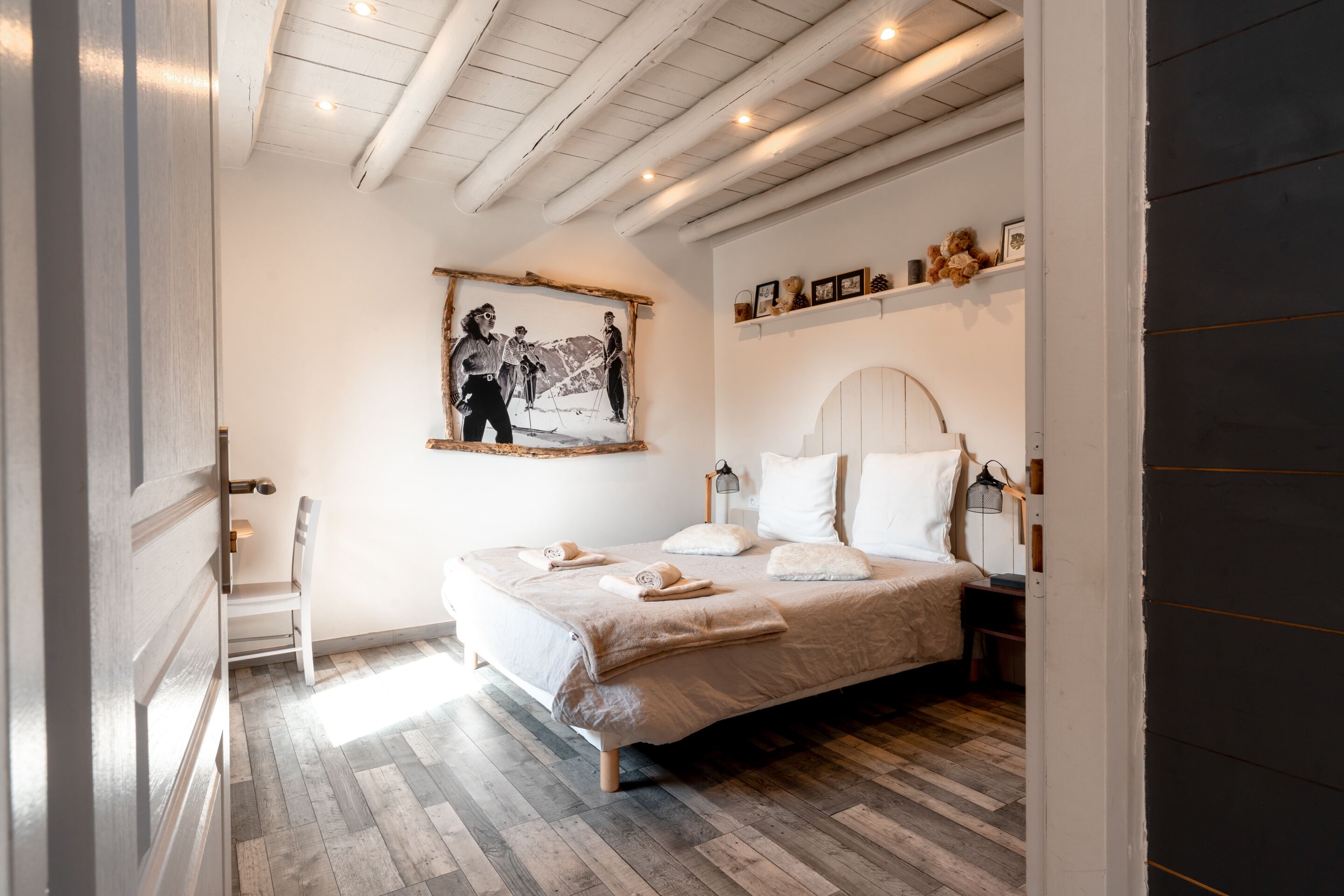 Un dormitorio con una cama, una silla, un cuadro en la pared y un estante con objetos pequeños.