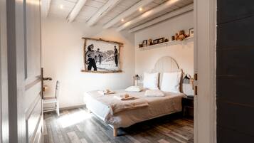 Un dormitorio con una cama, una silla, un cuadro en la pared y un estante con objetos pequeños.
