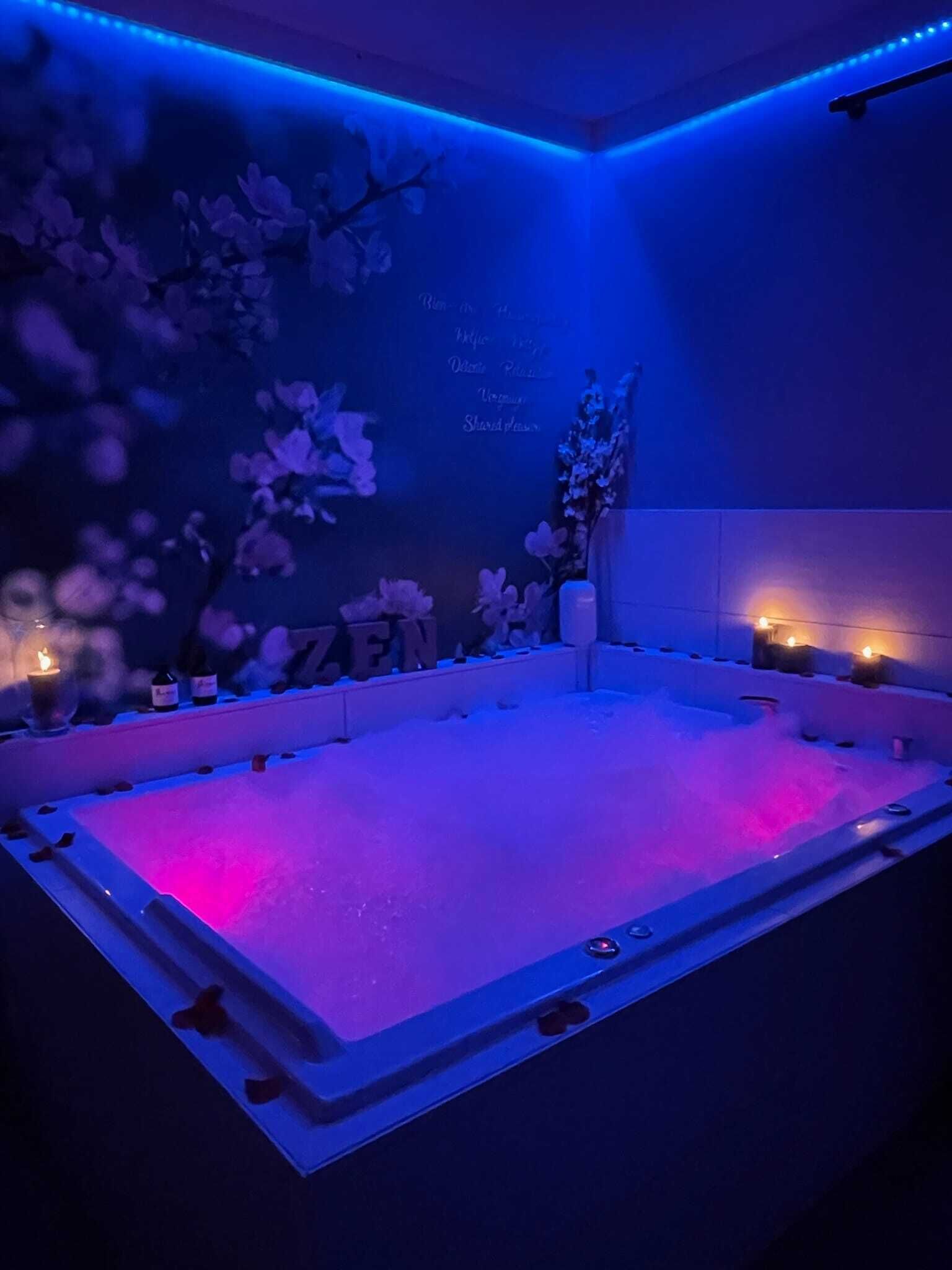A spa room with a large hot tub, floral decorations, and candles.