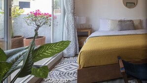 A bedroom with a bed, a bedside table, a hanging light fixture, and a view through a sliding door to the outside.