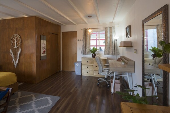 A modern bedroom with a wooden wardrobe, a desk with a chair, a bed with a yellow blanket, and a large mirror.