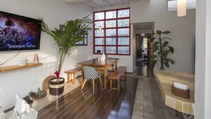 A spacious living area with a wooden dining table, benches, and a large window with red frames.