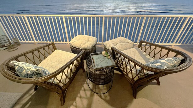 A balcony with wicker furniture and a view of the ocean at sunset.