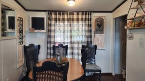 A dining area with a round table, six chairs, a plaid curtain, a wall-mounted TV, and a shelf with decorative items. - Animal Village/W/Mountain Views (Kalispell)