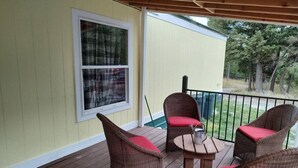 A covered porch with wicker chairs and a table, a window, and a view of trees. - Animal Village/W/Mountain Views (Kalispell)