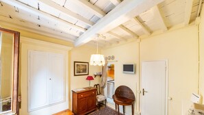 Een kamer met een houten plafond, een witte deur, een houten kast, een stoel, een klein tafeltje en een kamerkleed met dessin.