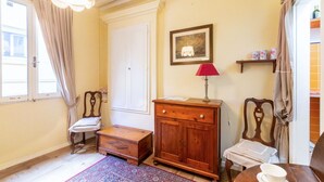 Een kamer met een houten kast, een stoel, een kleine tafel met een kopje, een vloerkleed en een kroonluchter.