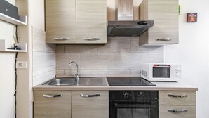 Una cucina moderna con pensili in legno chiaro, lavello in acciaio inossidabile, microonde integrato e forno nero.