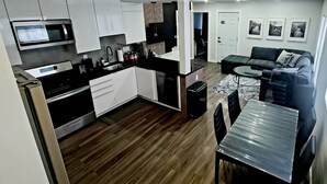 A modern kitchen with white cabinets, a black countertop, and a built-in oven. There is a dining area with a table and chairs, and a living room with a sofa and a coffee table. - Contemporary 3 bedroom apartment on the first floor overlooking the Salmon River (Pulaski)