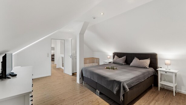 A modern bedroom with a sloped ceiling, a large bed, a bedside table with a lamp, and a TV on a white cabinet. - Gorgeous home in Loxstedt with WiFi (Loxstedt)