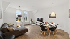 A modern living room with a sofa, coffee table, dining table with chairs, a TV, and artwork on the walls. - Gorgeous home in Loxstedt with WiFi (Loxstedt)