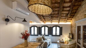 A cozy room with a wooden ceiling, a dining table with woven placemats, a wicker chair, and a sofa.