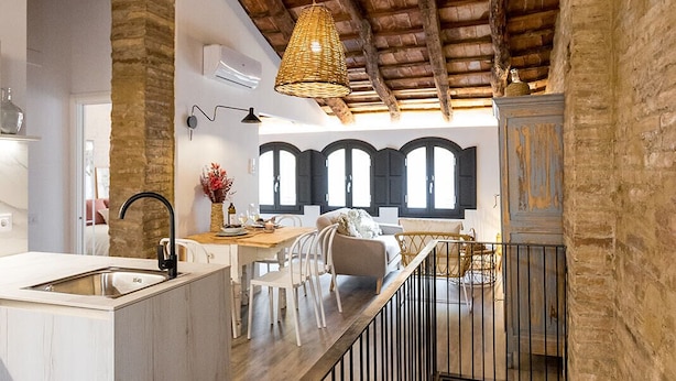 A modern kitchen with a central island, wooden beams, and a hanging light fixture.