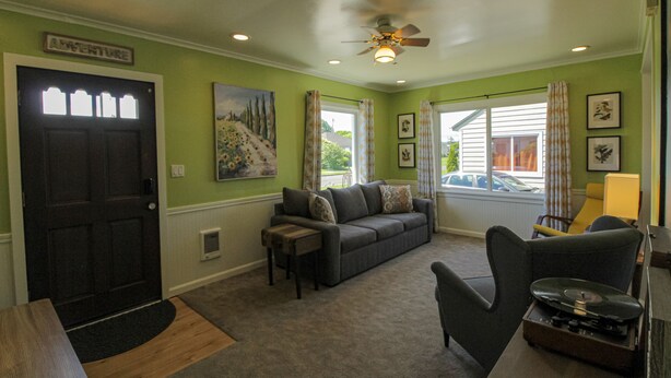 A living room with a dark door, a gray sofa, a small table, and a ceiling fan. - Work away ready, dog friendly. Downtown Tillamook - Modern Vintage (Tillamook)