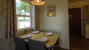 A dining area with a table set for four, a window with curtains, a painting on the wall, and a door leading to another room. - Work away ready, dog friendly. Downtown Tillamook - Modern Vintage (Tillamook)