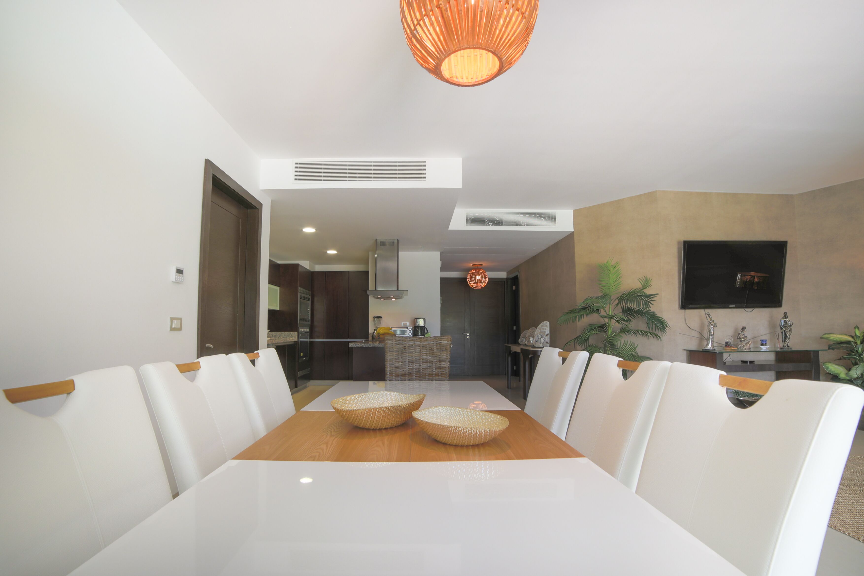 A modern dining area with a white table and chairs, a wooden floor, and a kitchen in the background.