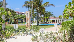 A beachside resort with palm trees, a pool, and a playground. - Marea Azul Beach Resort  (Playa del Carmen)
