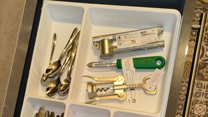 Eine Schublade mit Fächern, die verschiedene Küchenutensilien wie Löffel, Gabeln, Messer und einen Flaschenöffner enthalten.