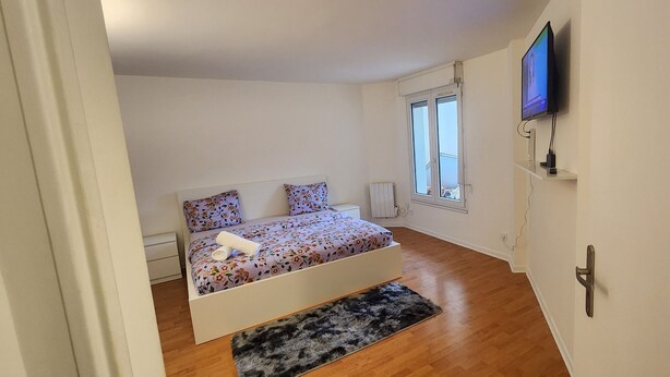 Ein Schlafzimmer mit einem Bett, einem an der Wand montierten Fernseher, einem Fenster und einer Heizung.