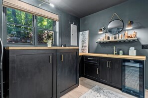 A modern kitchen with dark cabinetry, a built-in dishwasher, and a window overlooking greenery.