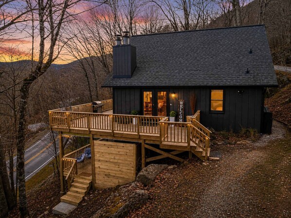 A cabin with a deck, a chimney, and a 'WELCOME' sign.