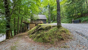 Een chalet met een houten terras en een trap naar een deur, omgeven door bomen en een grindpad.