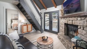 A modern living room with a fireplace, a staircase, and a large window.