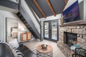 A modern living room with a fireplace, a staircase, and a large window.