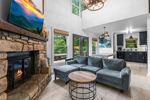 A spacious living area with a stone fireplace, a gray sectional sofa, and a round wooden coffee table.