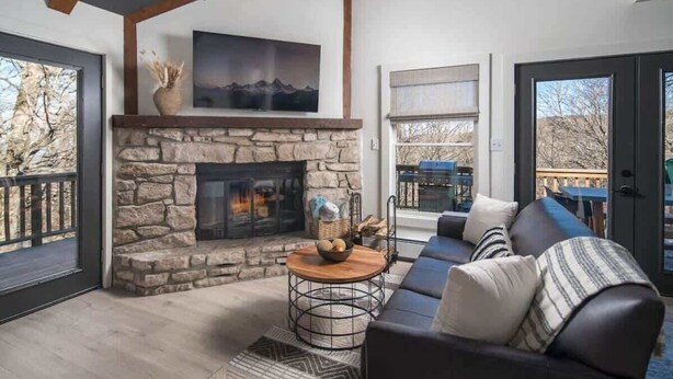 A living room with a stone fireplace, a sofa, a coffee table, and a view of the outdoors.