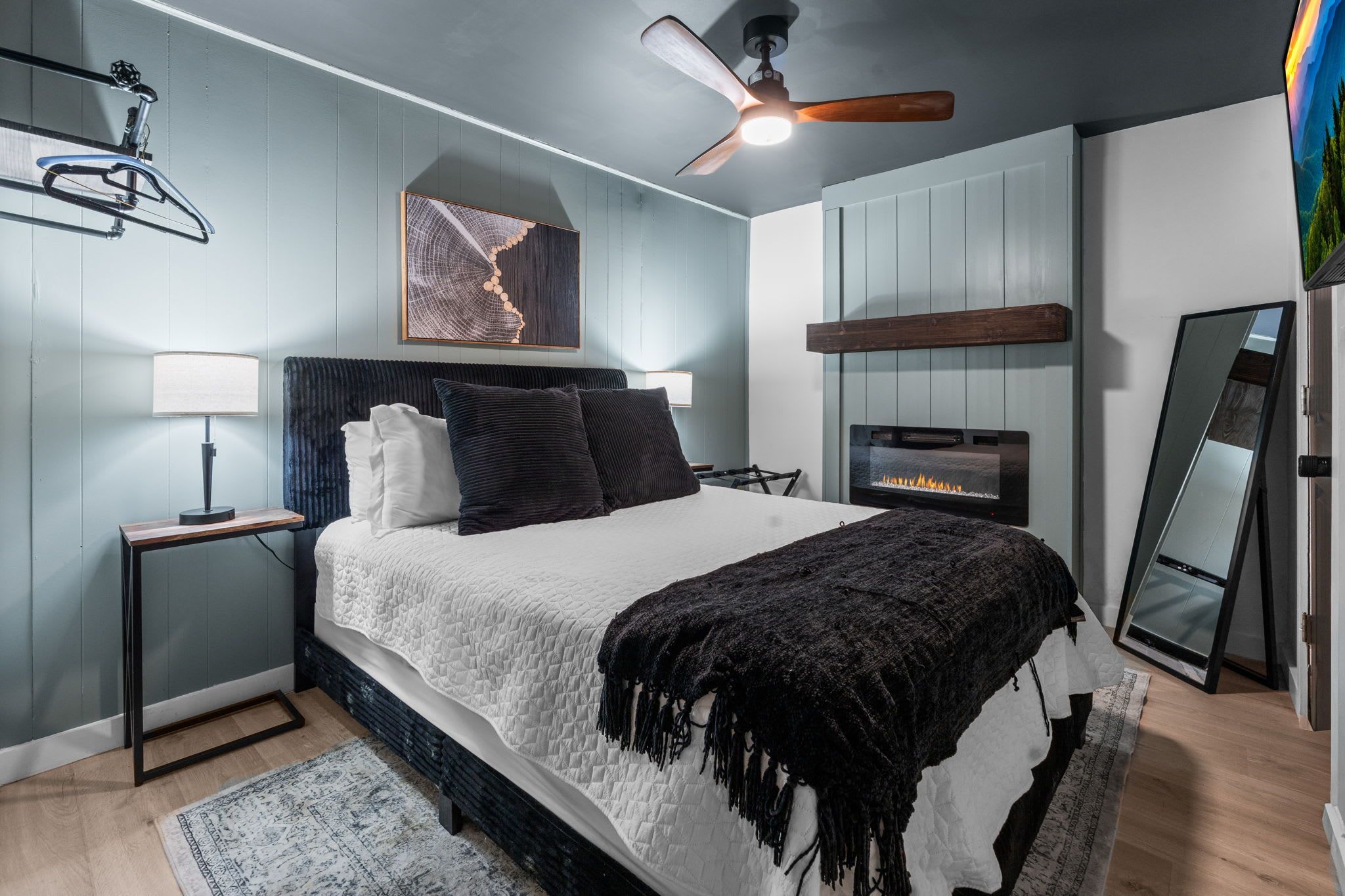 Quarto moderno com cama, mesas de cabeceira, ventilador de teto, lareira e espelho.