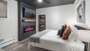A bedroom with a bed, a TV mounted on the wall, and a fireplace.