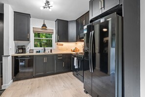 A modern kitchen with dark cabinetry, a stainless steel refrigerator, a built-in oven, and a coffee maker.