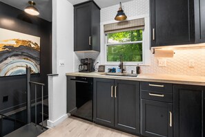 A modern kitchen with dark cabinetry, a window with a view of greenery, and a coffee maker on the counter.