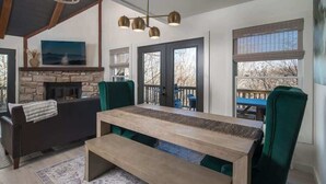 A living room with a fireplace, a large wooden table, and green chairs.