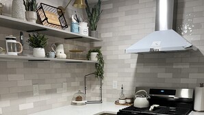 Una cocina moderna con armarios grises, estufa de acero inoxidable y salpicadero de azulejos blancos.