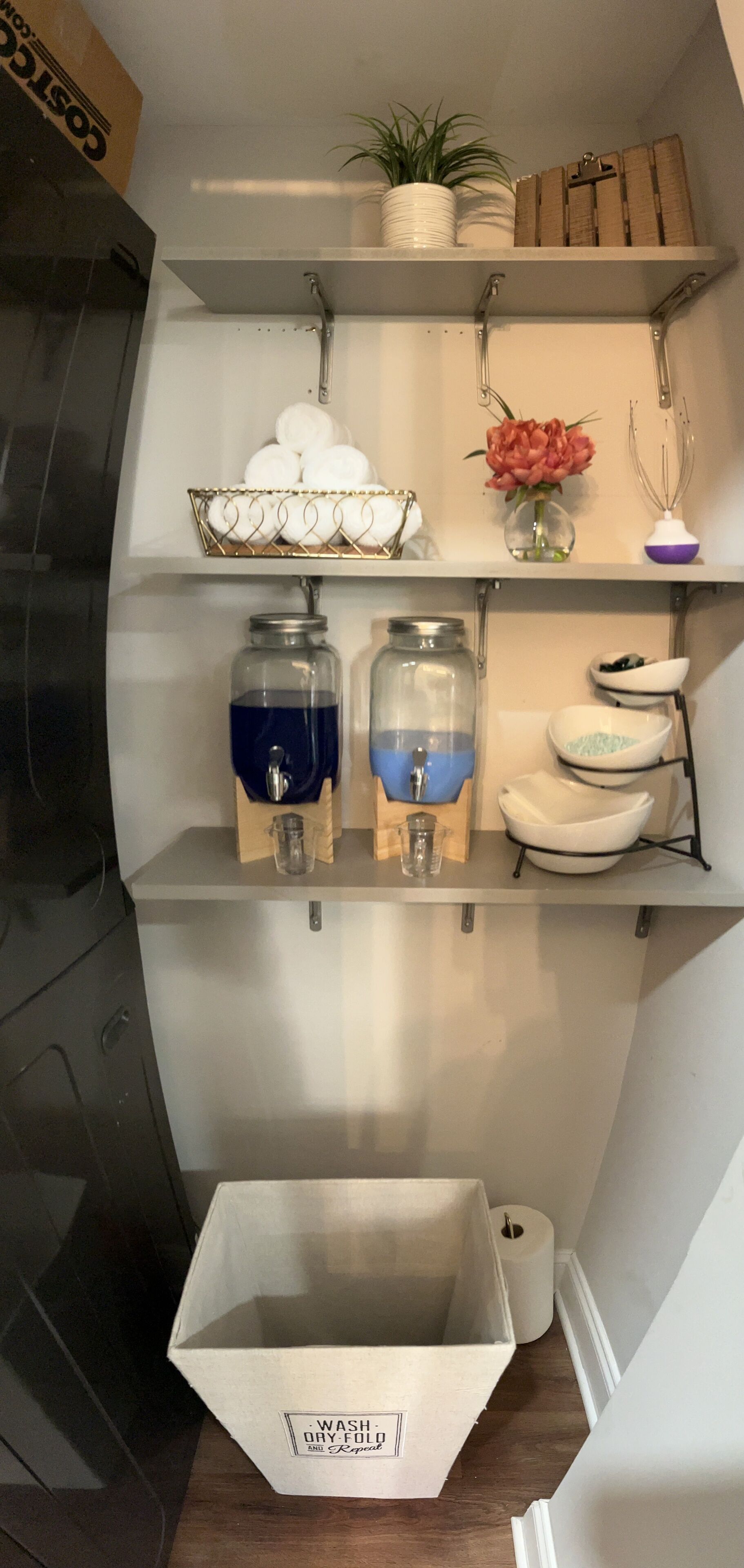 A kitchen with shelves holding jars, a plant, and a white box labeled "WASH-DRY-FOLD."