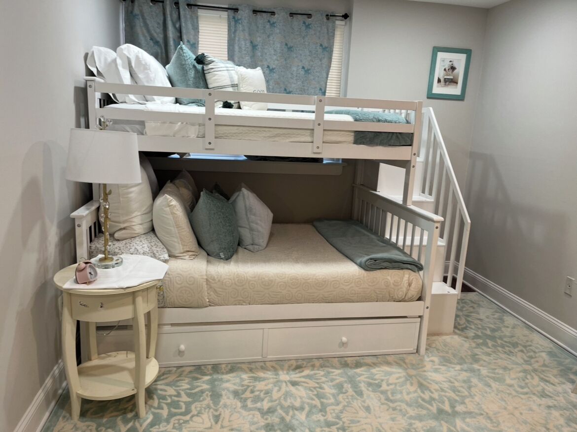 Un letto a castello con una scrivania e una sedia, una lampada e un tavolino con una cornice.