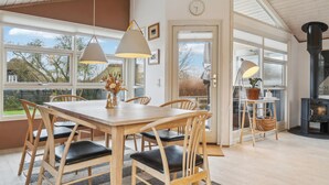 A dining area with a wooden table and chairs, pendant lights, and a view through large windows. - 3 bedroom pet friendly home in Beder (Beder)