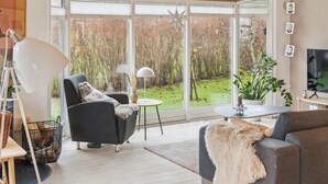 A modern living room with a large window, a black armchair, a round table, and a television. - 3 bedroom pet friendly home in Beder (Beder)