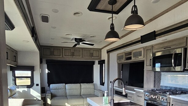 A compact RV kitchen with a central island, a ceiling fan, and a microwave.