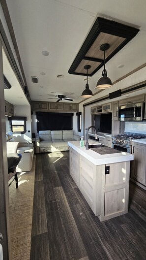 A compact RV kitchen with a central island, a ceiling fan, and a microwave.