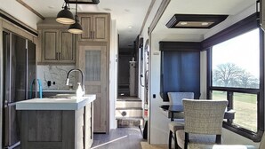 A modern RV interior with a kitchen area, a dining space, and a seating area with a view.