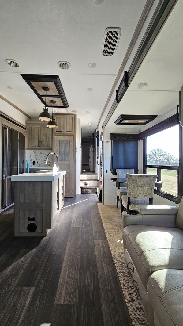 A modern RV interior with a kitchen area, a dining space, and a seating area with a view.