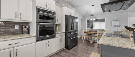A modern kitchen with white cabinetry, stainless steel appliances, and a dining area with a wooden table and chairs.