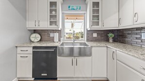 Una cocina con gabinetes blancos, un lavamanos de acero inoxidable y un lavavajillas.
