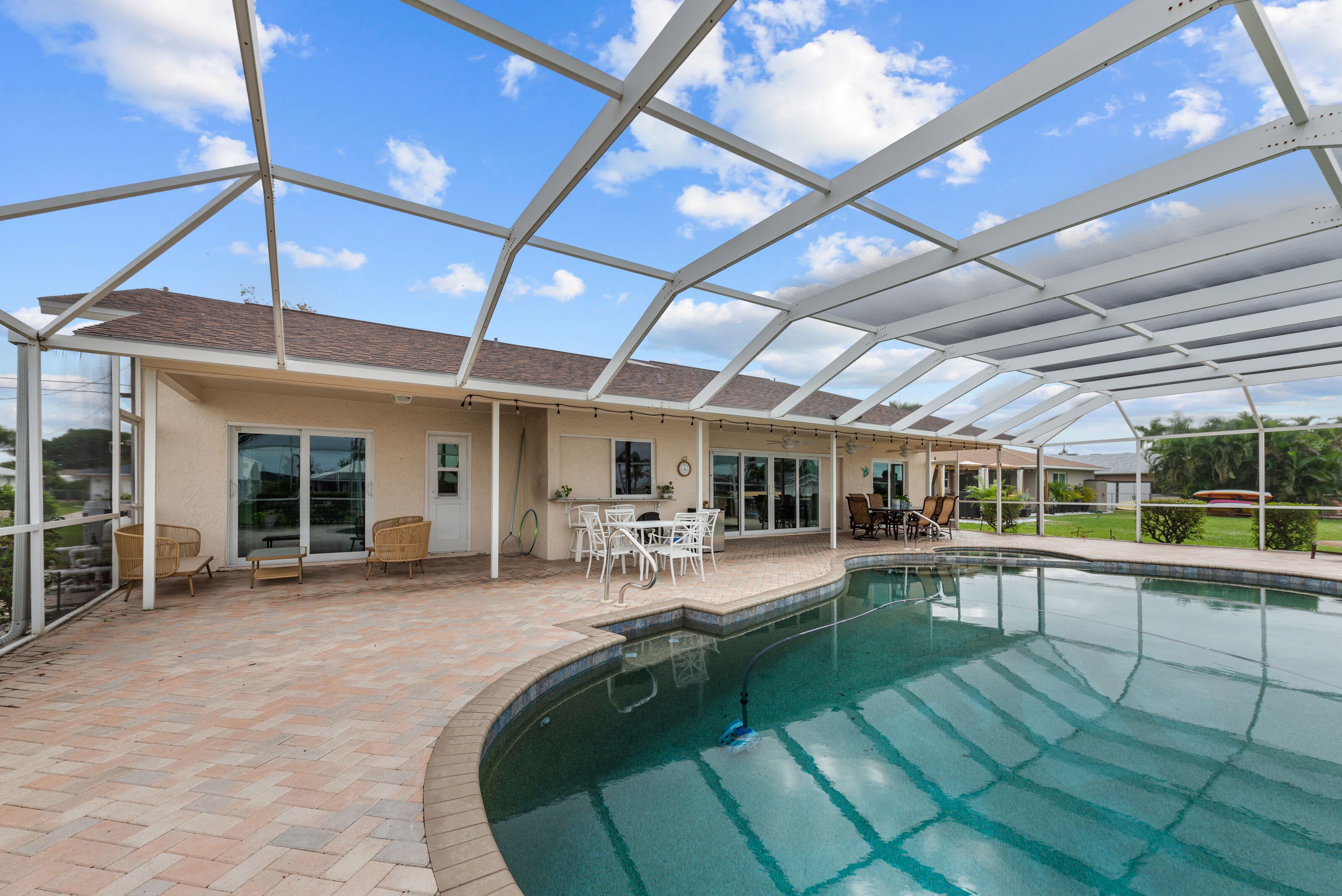 A covered swimming pool with a patio area, including outdoor seating and a view of the surrounding landscape.