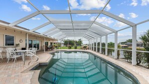 Una piscina techada con zona de patio, mobiliario exterior blanco y vistas del paisaje circundante.