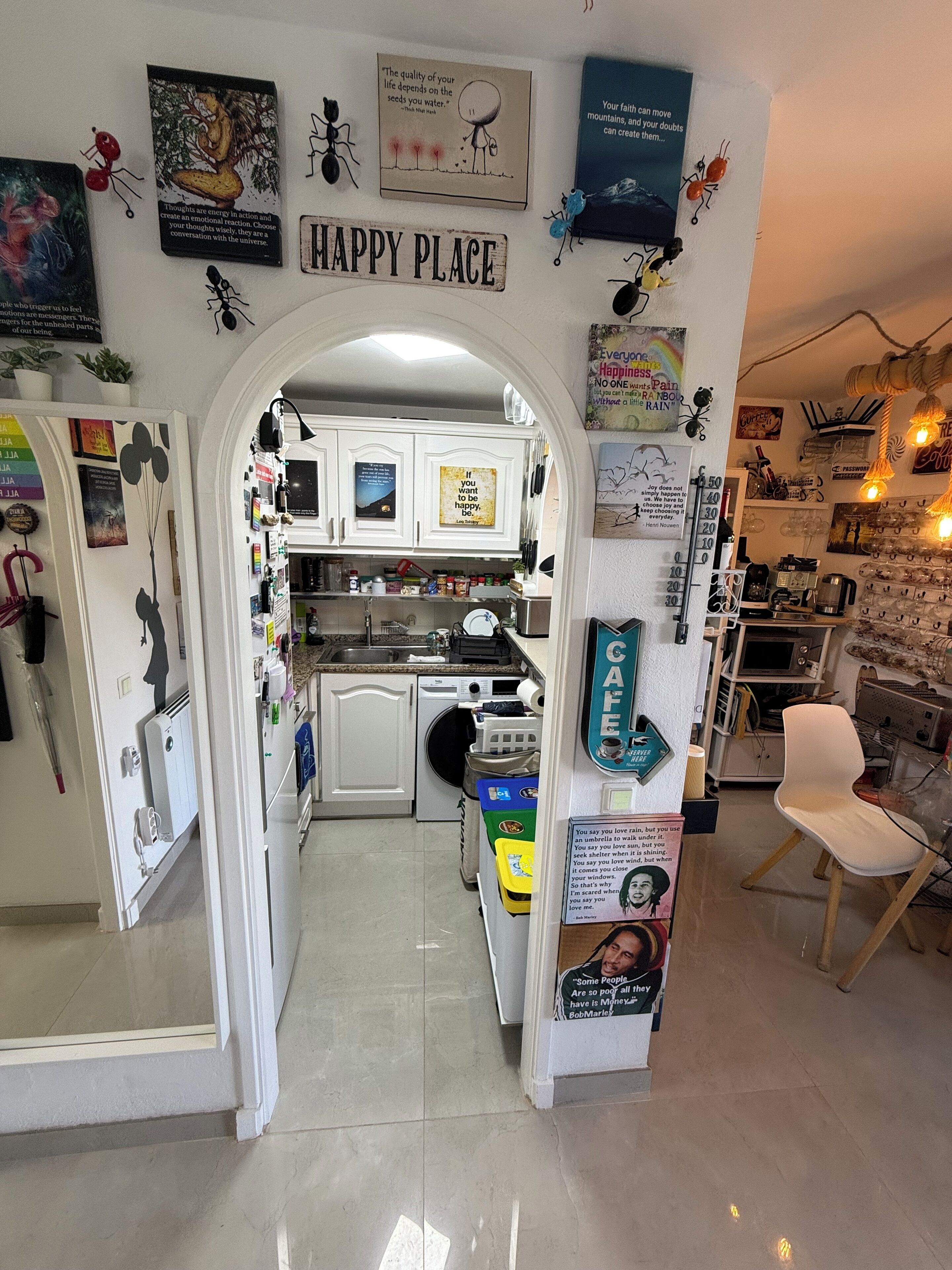 A kitchen with white cabinets, a stove, and various kitchen items. There are motivational posters on the walls, including one that says "HAPPY PLACE".